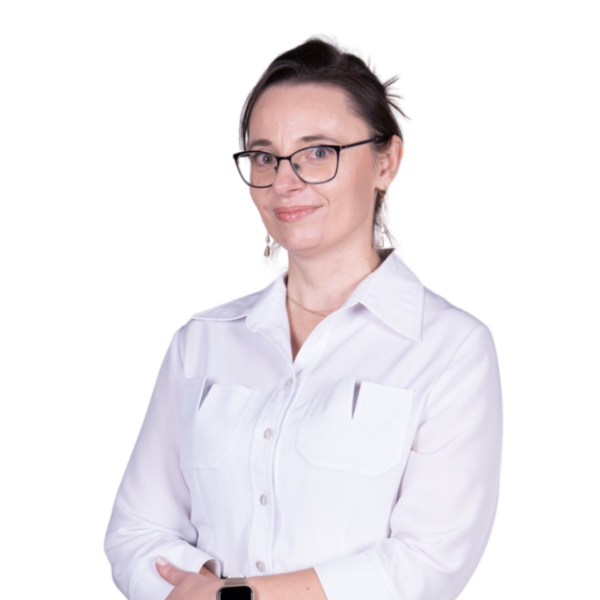 Portret kobiety w okularach i białej koszuli, stojącej na jasnym tle.