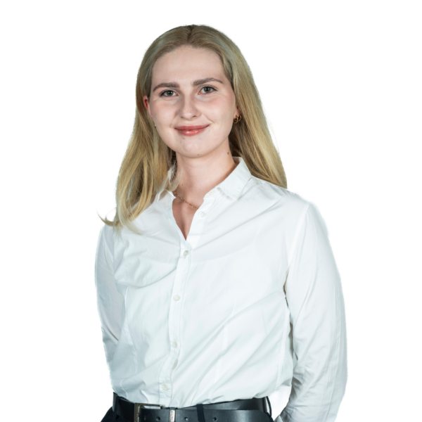Portret kobiety w białej koszuli, stojącej na jasnym tle i patrzącej w obiektyw.