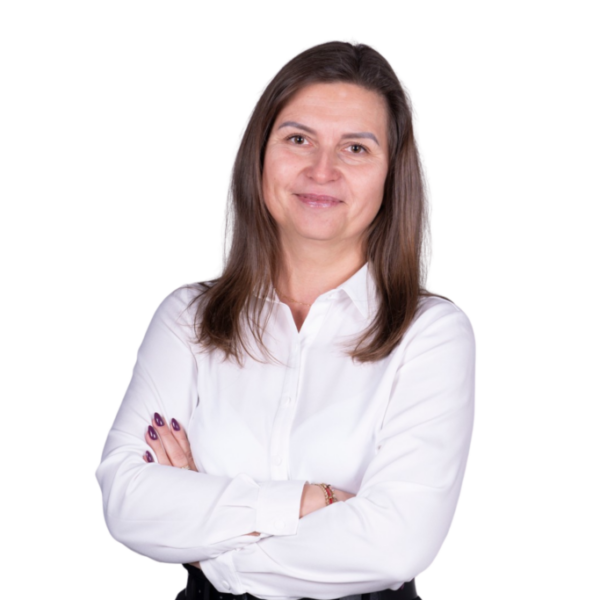 Portret kobiety w białej koszuli, stojącej ze skrzyżowanymi rękami na jasnym tle.
