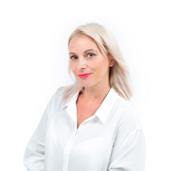 Portret blondynki w białej bluzce, pozującej na jasnym tle.