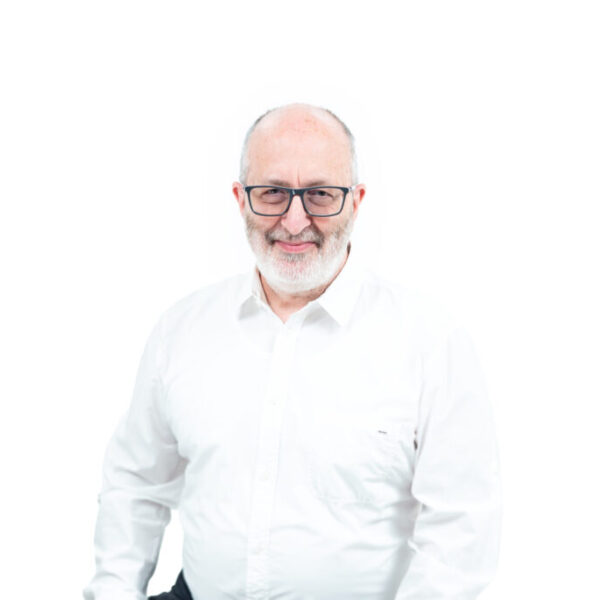 Portret uśmiechniętego mężczyzny z siwą brodą i w okularach, ubranego w białą koszulę, na jasnym tle.