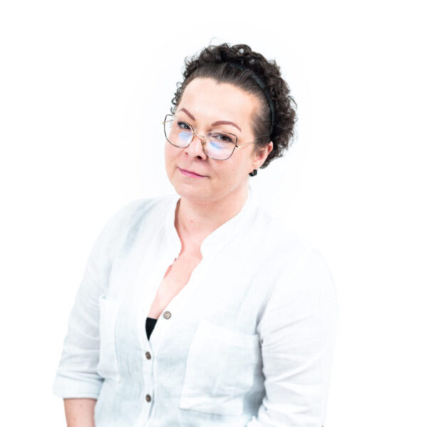 Portret kobiety w okularach i białej bluzce, pozującej na jasnym tle.