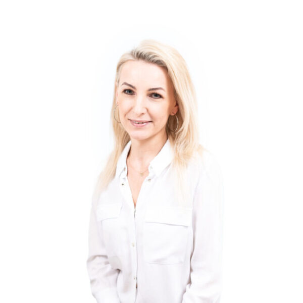 Portret blondynki w białej koszuli, pozującej na jasnym tle.