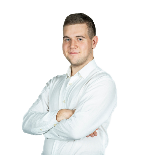 Portret młodego mężczyzny w białej koszuli, stojącego ze skrzyżowanymi rękami na jasnym tle.